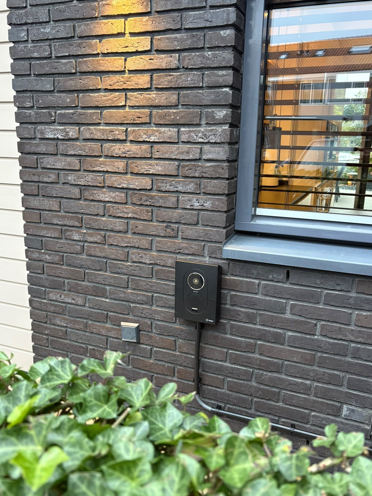 Zwarte Zaptec Go 2 laadpaal aan een donkere bakstenen gevel in Oegstgeest